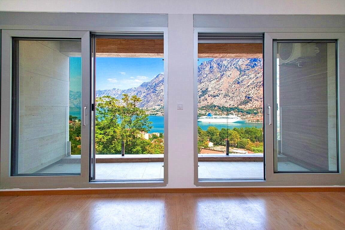 Panoramic view of the Bay of Kotor and the mountains from the living room of a modern apartment in Kotor, Montenegro, with access to the terrace.
