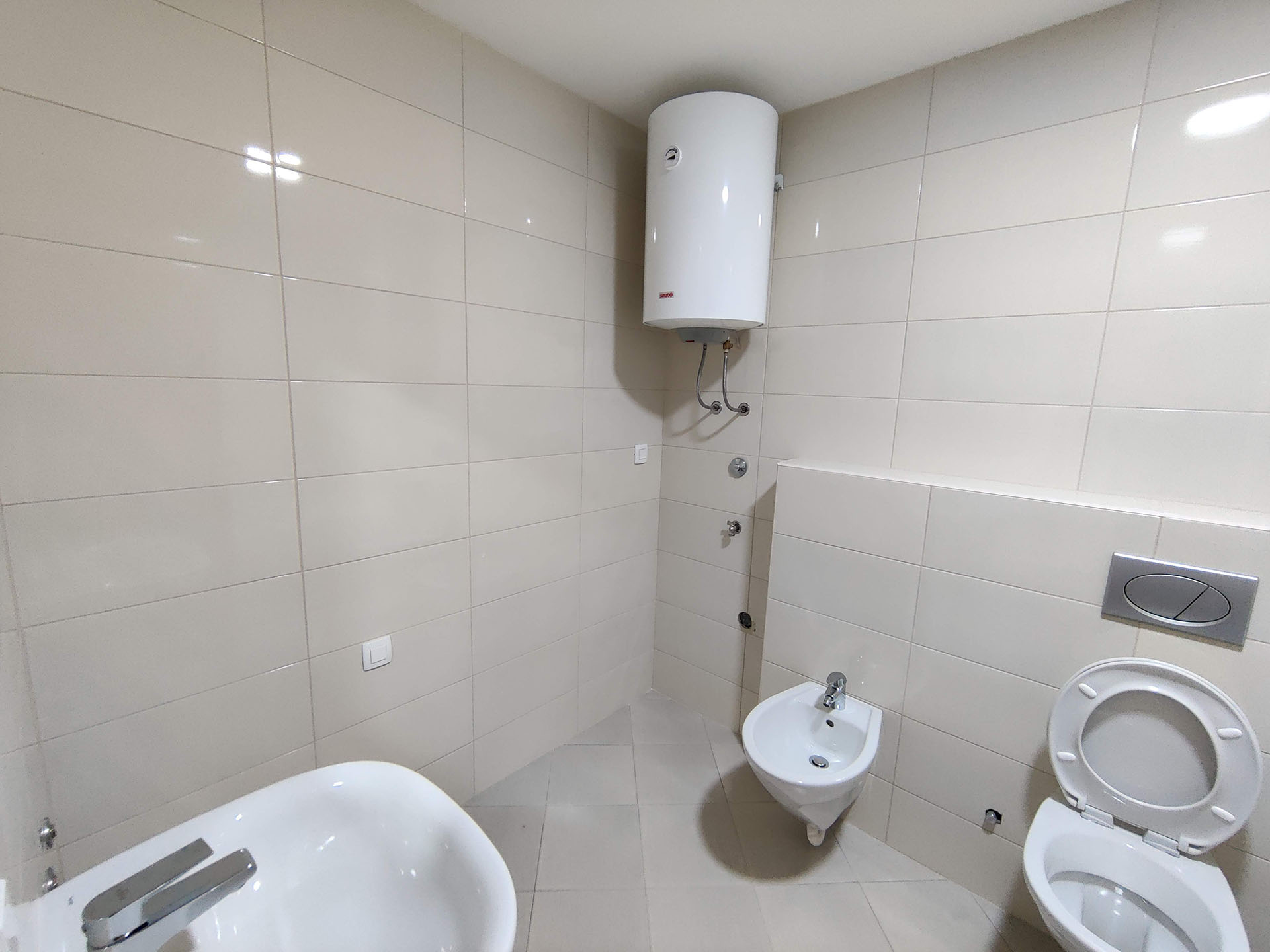 Bright bathroom in an apartment in Bečići, Montenegro: plumbing fixtures, bidet, toilet, and water heater on the wall.