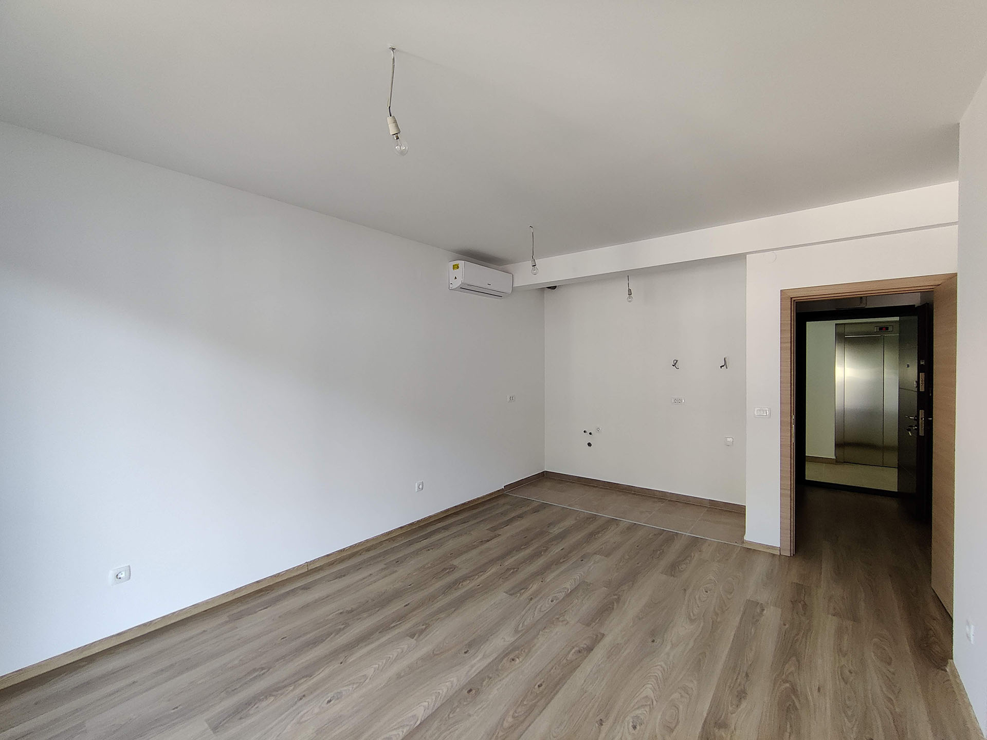 Bright living room in a new building in Bečići, Montenegro: laminate flooring, white walls, air conditioning, and access to the hallway with an elevator.