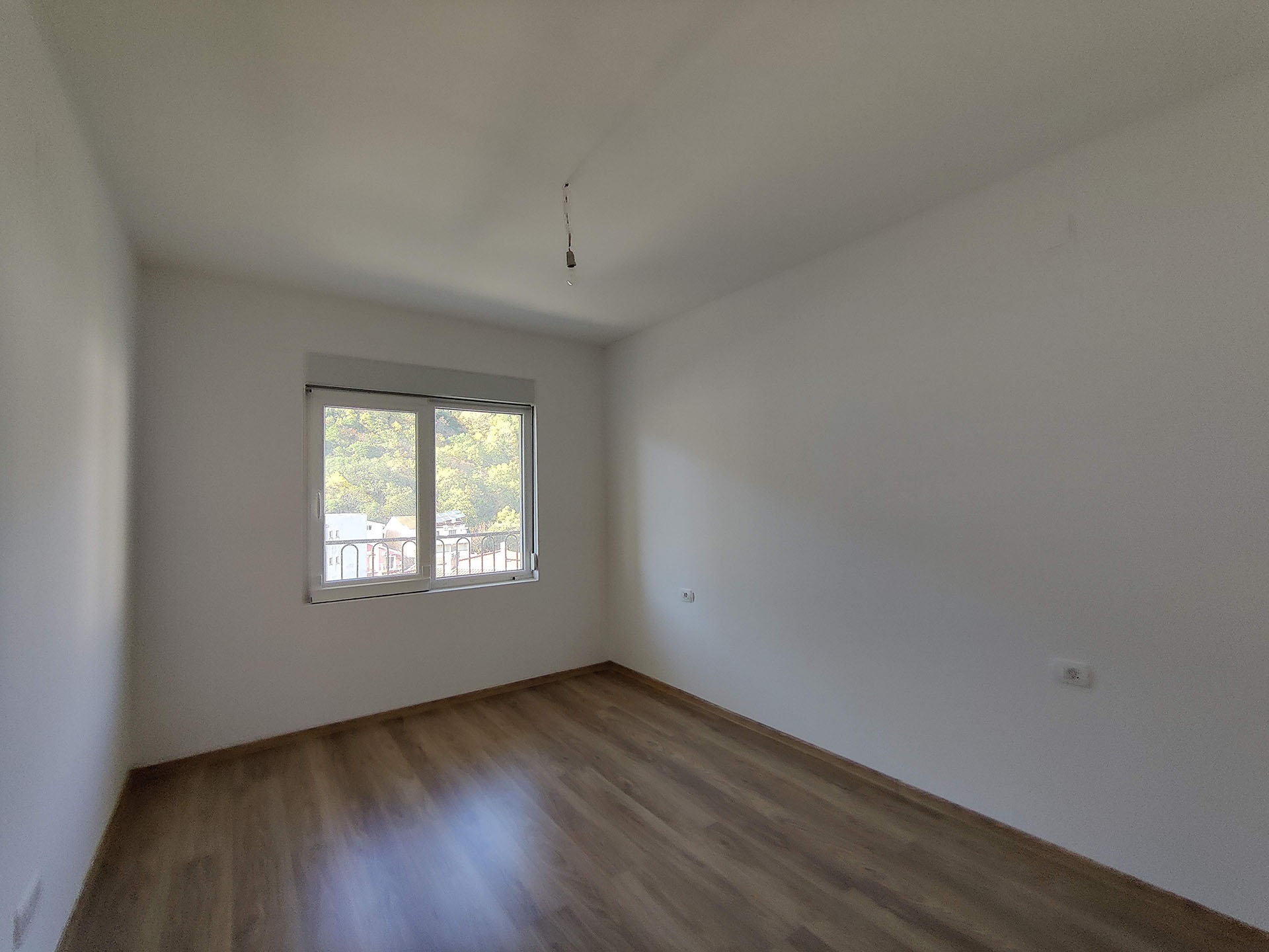 Bright bedroom with laminate flooring and mountain view in an apartment, Bečići, Montenegro. Empty room ready for finishing.