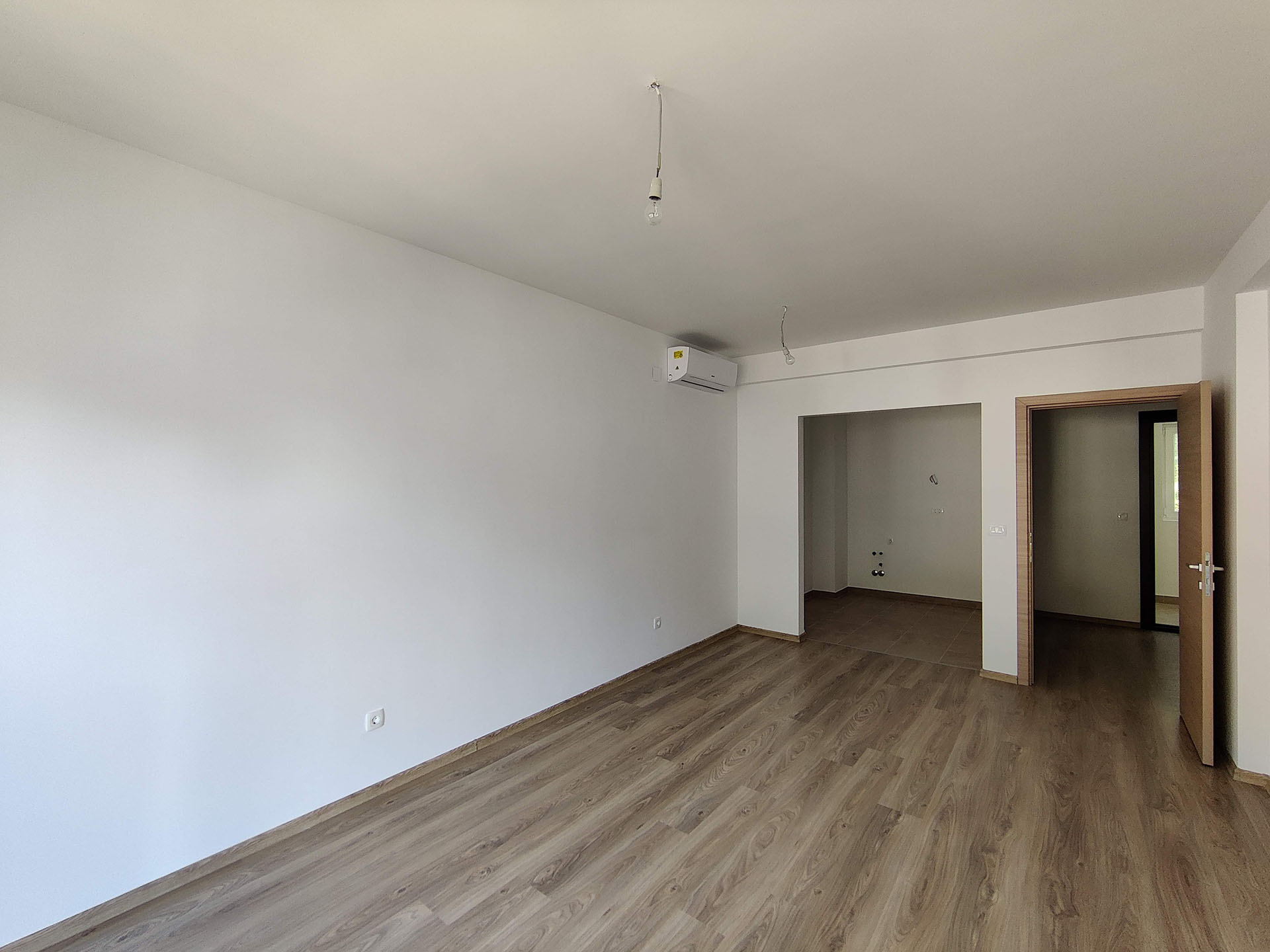 Bright living room with laminate flooring and air conditioning in a new apartment in Bečići, Montenegro, view of the kitchen area and hallway.
