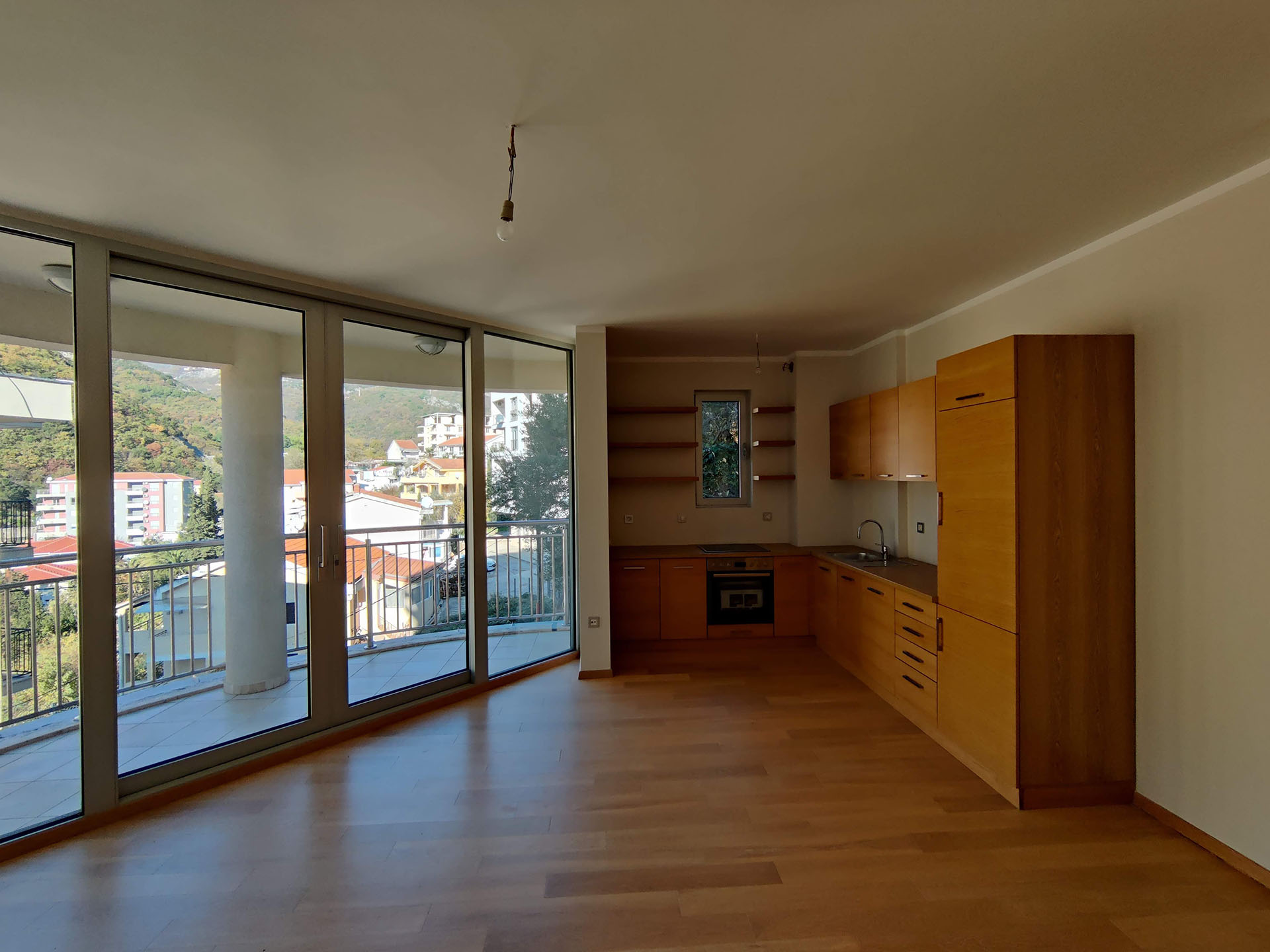 Kitchen with wooden cabinetry and panoramic windows in an apartment in Bečići, Montenegro, overlooking the mountains and the city.