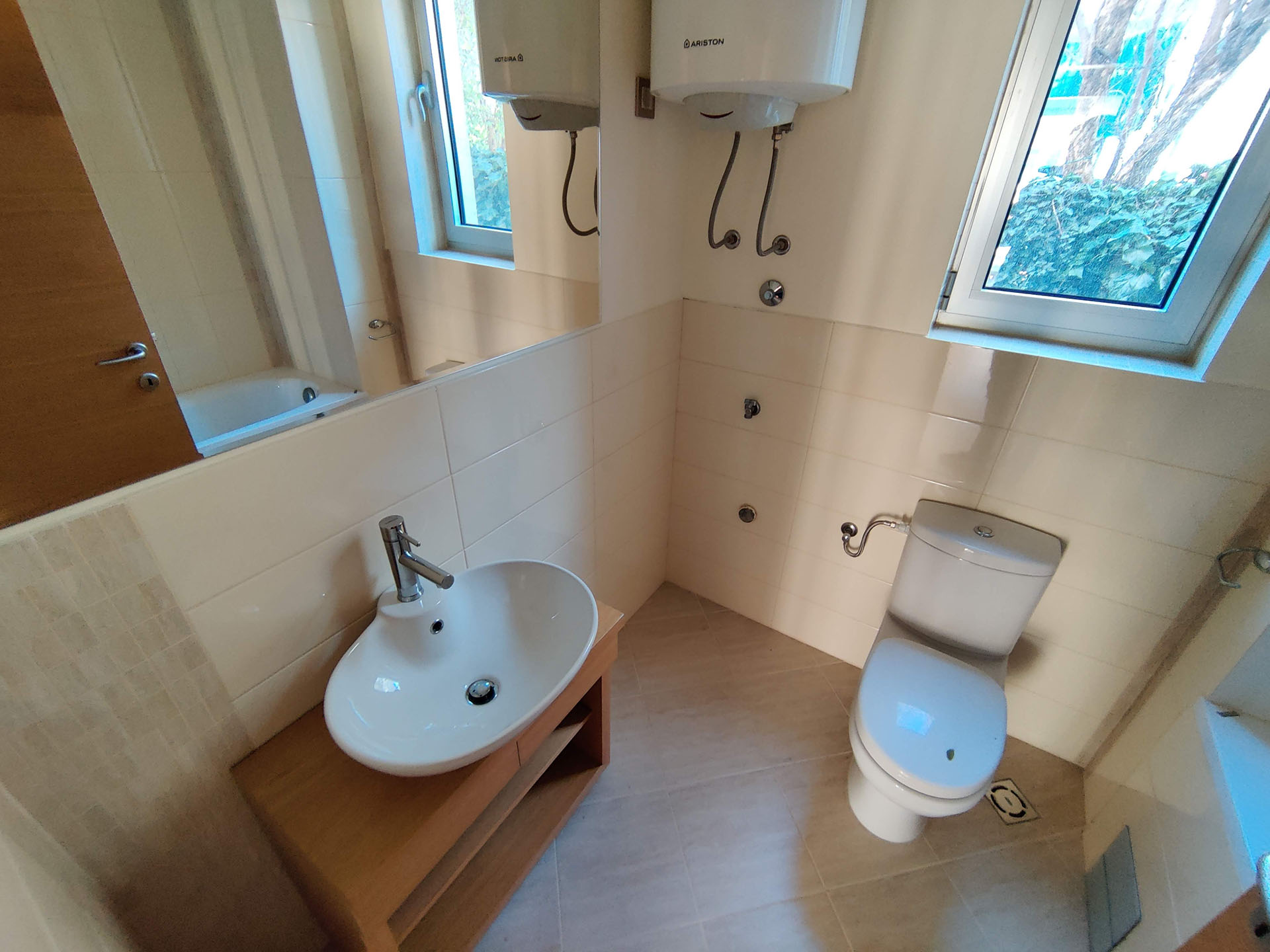 Bright bathroom in an apartment in Bečići, Montenegro: a sink on a wooden vanity, a toilet, and an Ariston water heater.