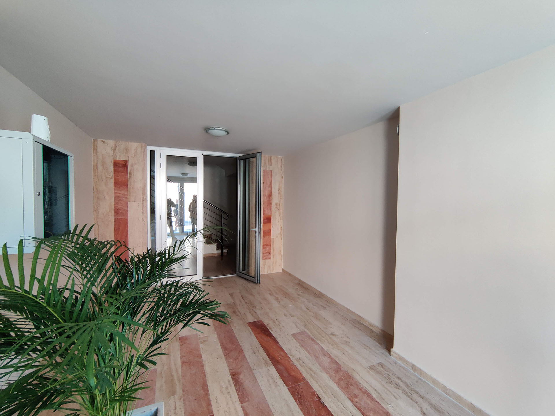 Bright hallway with stone finishes and a live plant in a residential complex in Bečići, Montenegro.