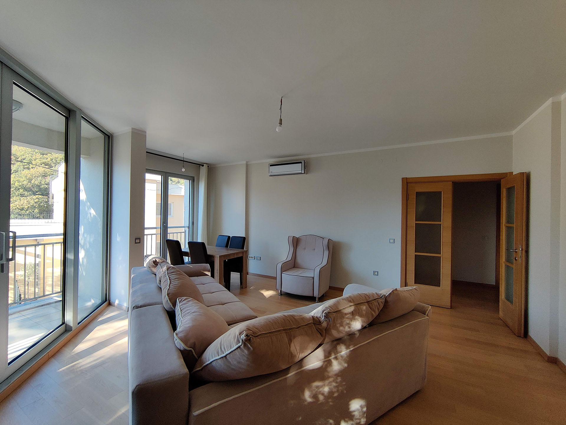 Bright living room with panoramic windows and furniture in an apartment in Bečići, Montenegro. Parquet flooring, dining area, and balcony.