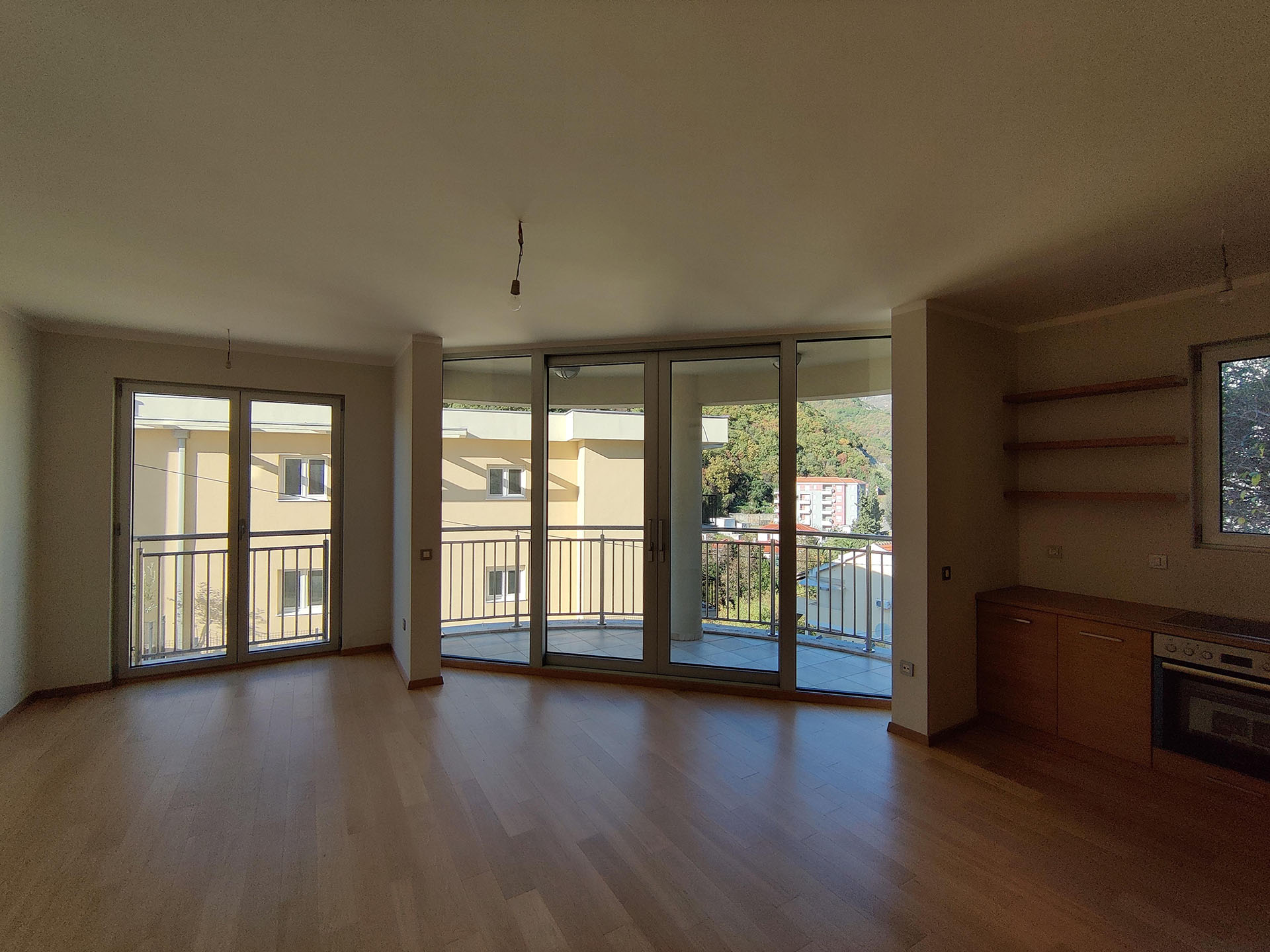 Bright living room with panoramic windows and kitchen in an apartment, Bečići, Montenegro. View of the mountains and terrace, parquet flooring.