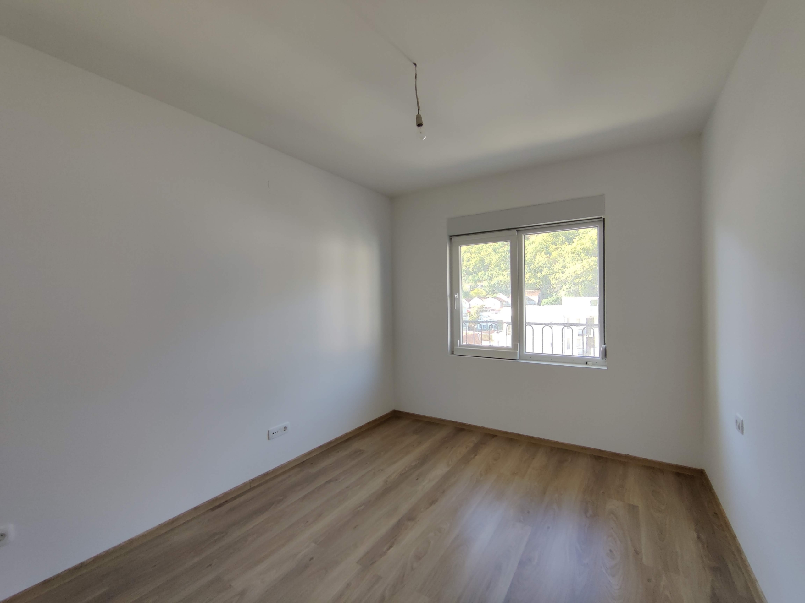 Bright unfurnished bedroom with laminate flooring and a window in an apartment for sale in Bečići, Montenegro.