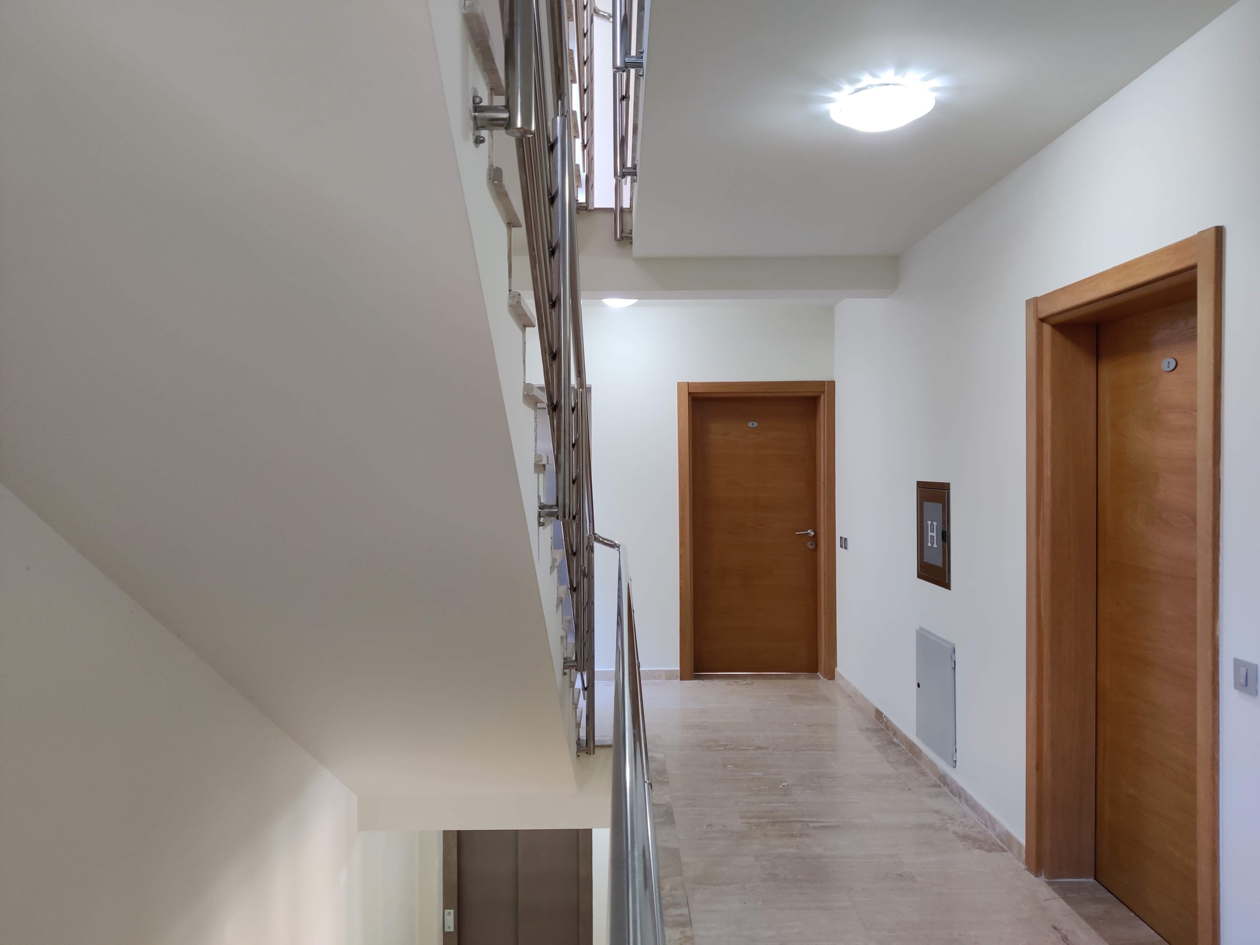 Bright corridor and staircase with metal railings in a residential complex in Bečići, Montenegro. Wooden interior doors.