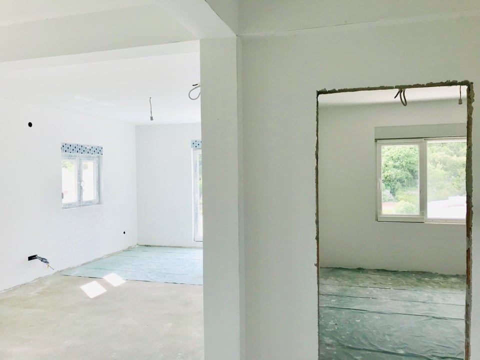 Bright living room under renovation in an apartment, Bečići, Montenegro: white walls, plastic windows, and floor screed.