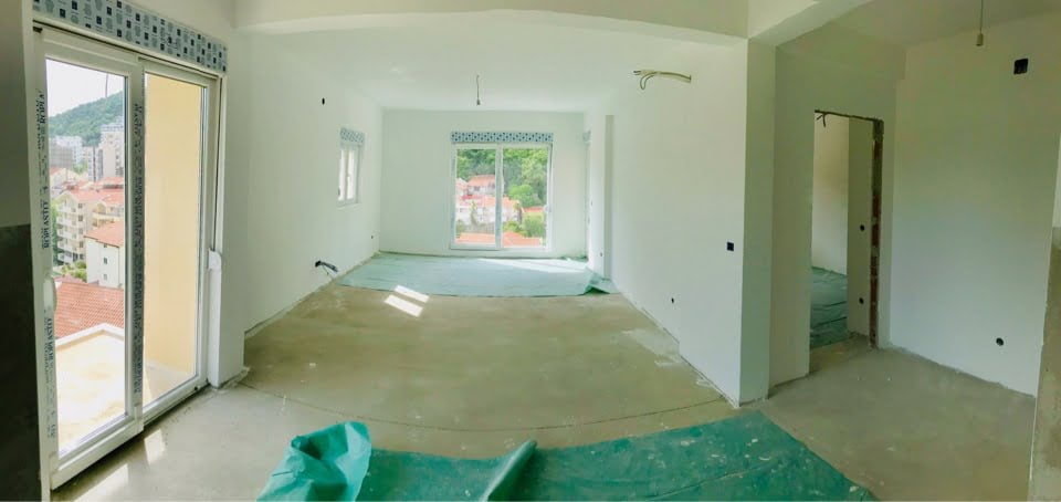 Spacious unfinished living room in a new building, Bečići, Montenegro: panoramic windows and a view of the mountains and the city.