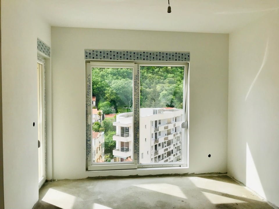 Living room in a new building in Bečići, Montenegro: a bright room with a panoramic window and a view of the mountains and the city.