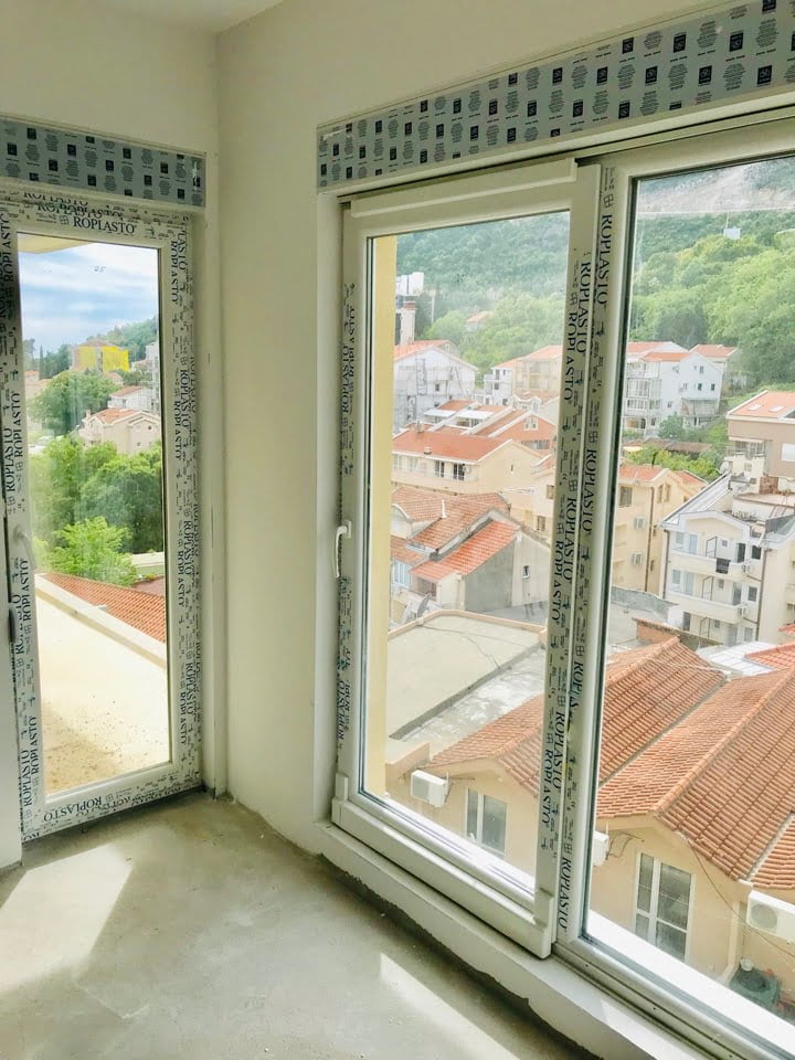View from the living room window of tiled roofs and mountains in Bečići, Montenegro. New PVC windows in a bright apartment.