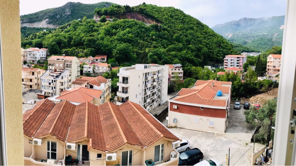 View from the apartment balcony in Bečići, Montenegro: a panorama of residential buildings with tiled roofs and green mountains.