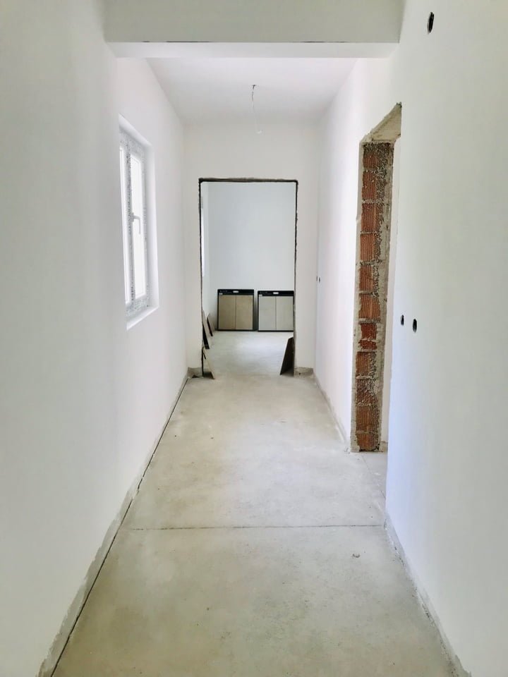 Hallway in an apartment under construction in Bečići, Montenegro: white walls, concrete floor, and an opening into the adjacent room.