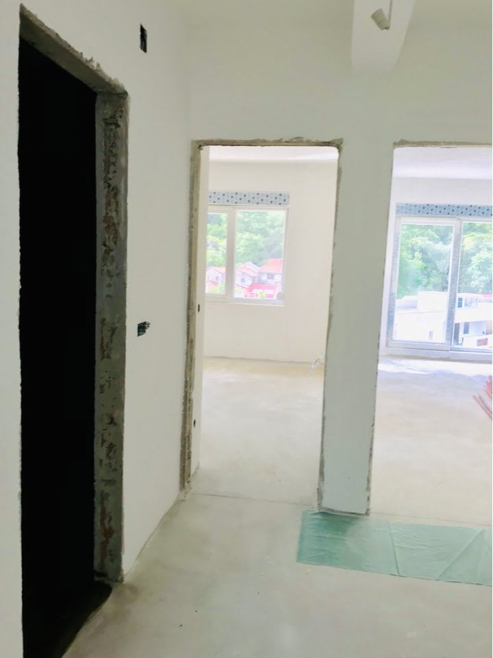 Living room in an unfinished apartment in Bečići, Montenegro: light walls, doorways, and a view of greenery from the windows.