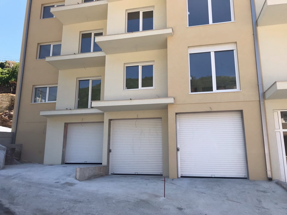 Facade of a new residential building with garage roller shutters in Bečići, Montenegro: modern finish and panoramic windows.