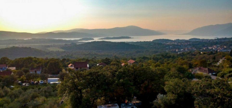Panoramic view of the mountains and bay from a residential complex in Kavac, Montenegro: a picturesque landscape with greenery at sunset.