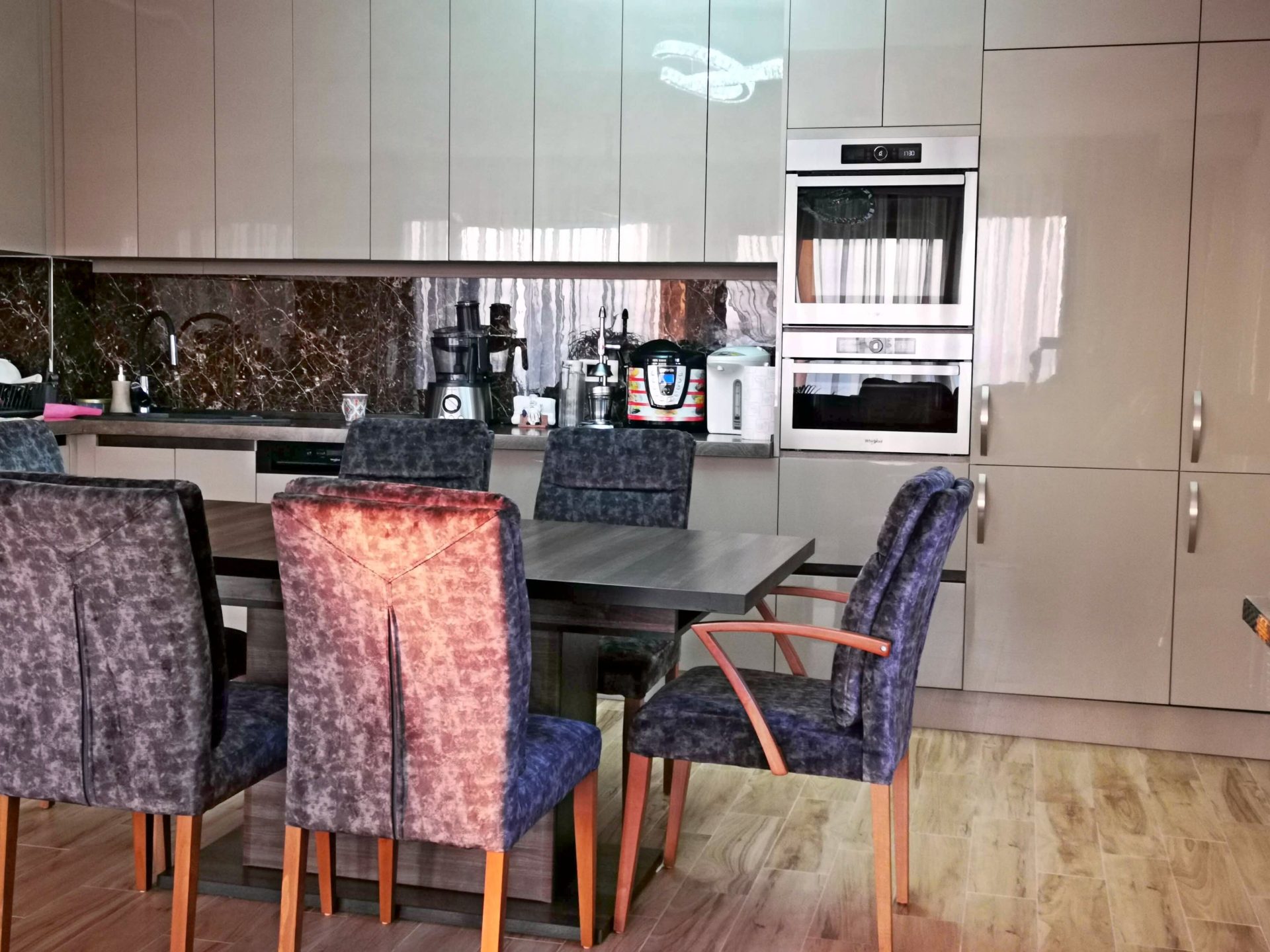 Modern kitchen with dining area in a villa in Bar, Montenegro: glossy fronts, built-in appliances, and soft chairs.