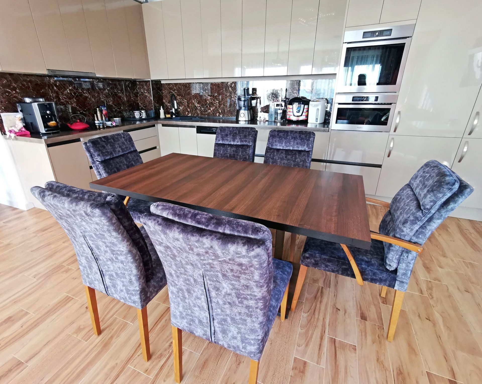 Modern kitchen with dining area in a villa in Bar, Montenegro: glossy cabinets, dark backsplash, and upholstered chairs.