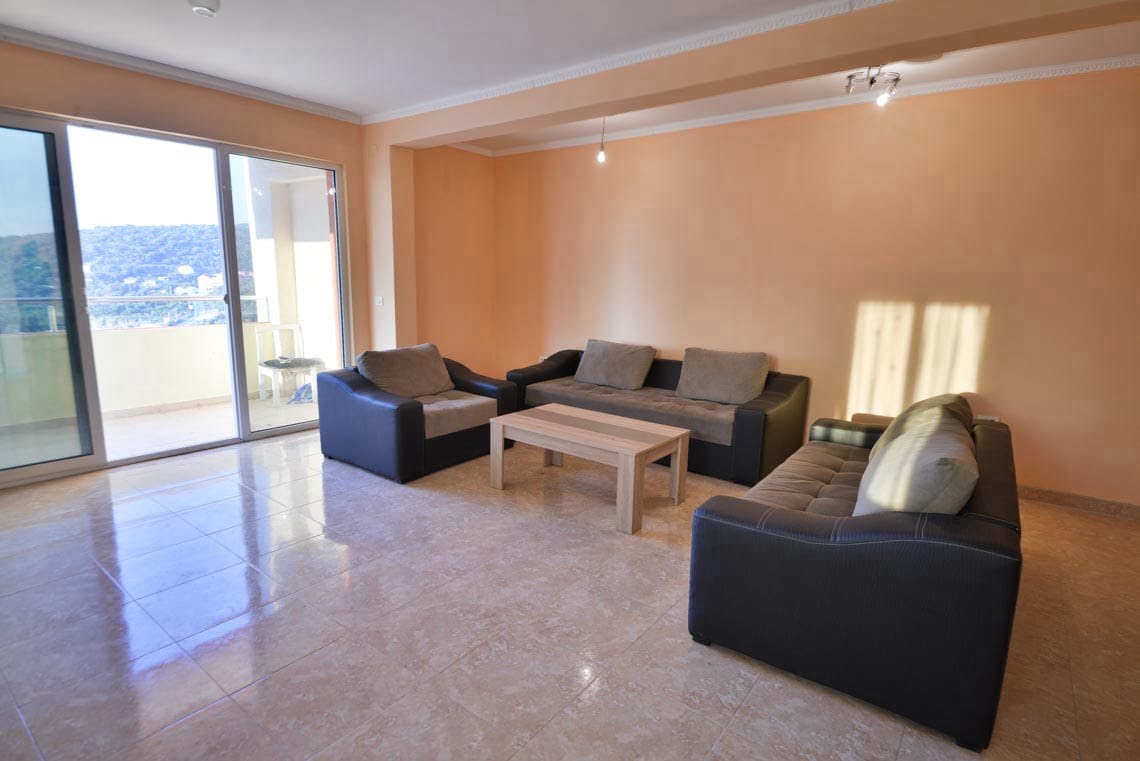 Living room in an apartment in Utjeha, Montenegro: soft furniture, tiled floor, and a panoramic exit to a terrace with sea view.