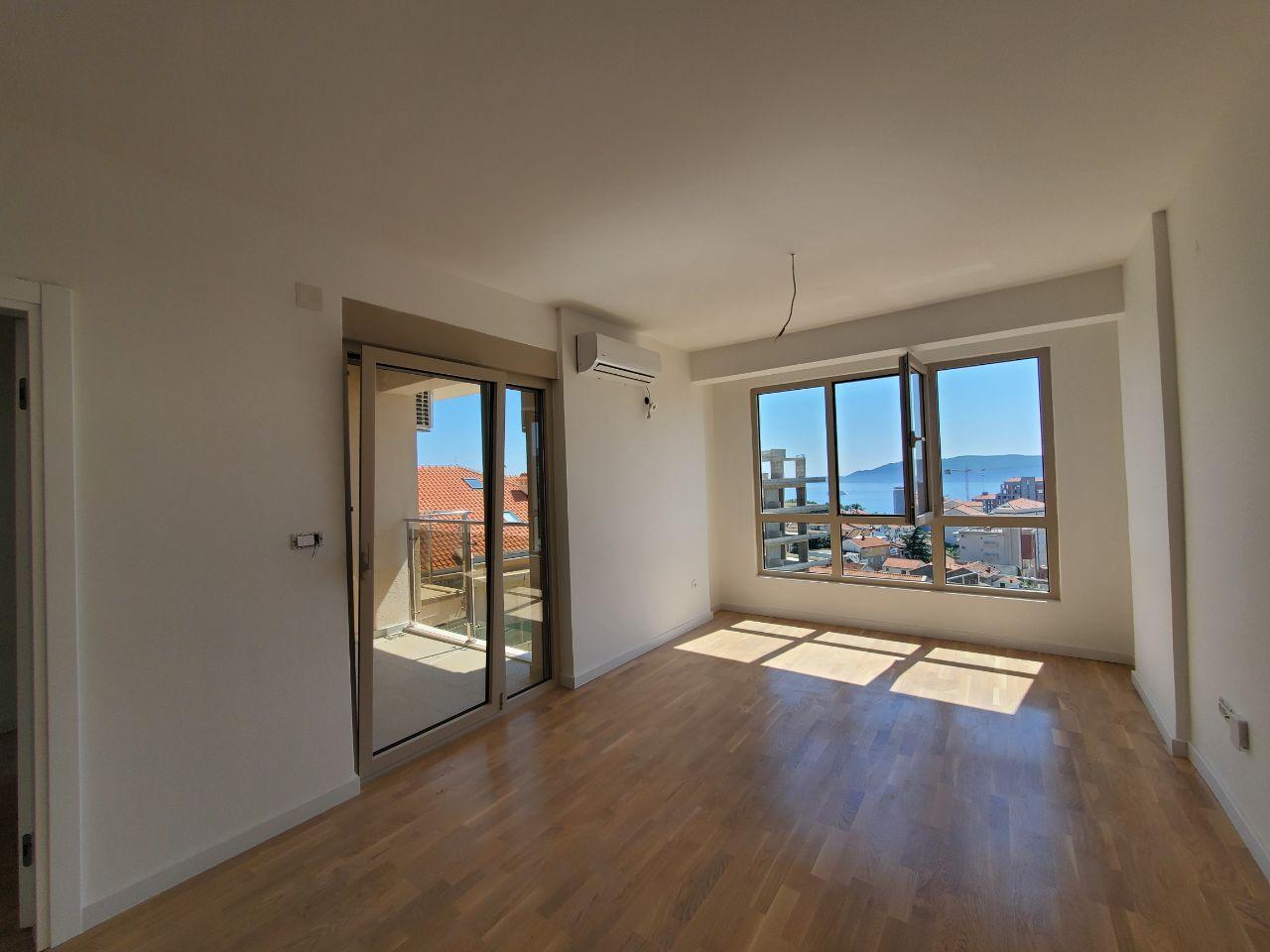 Bright living room with parquet flooring and access to the balcony in a residential building in Bečići, Montenegro, with panoramic sea views.