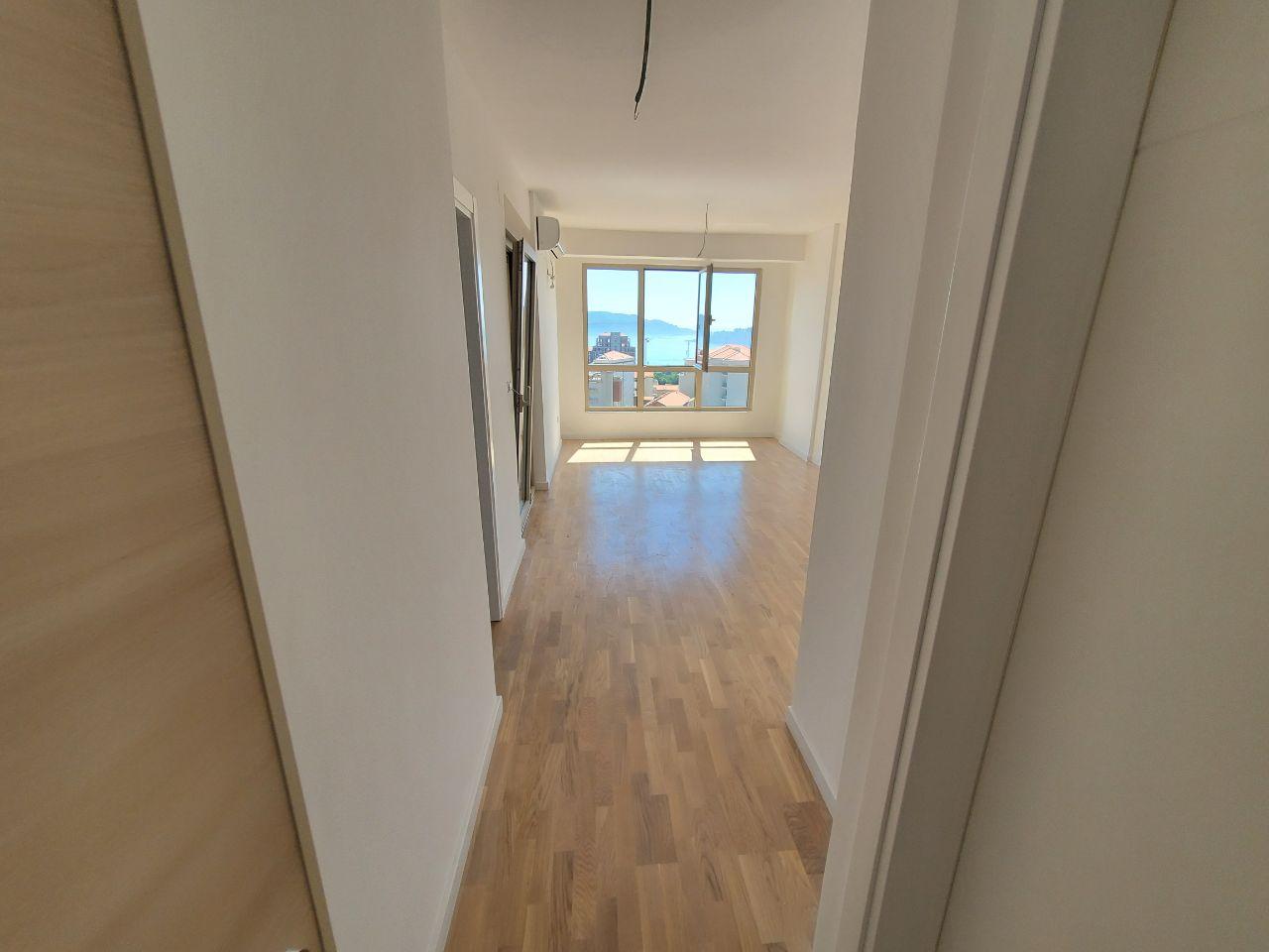 Bright living room with parquet flooring in a new building in Bečići, Montenegro, sea and mountain view from the panoramic window.