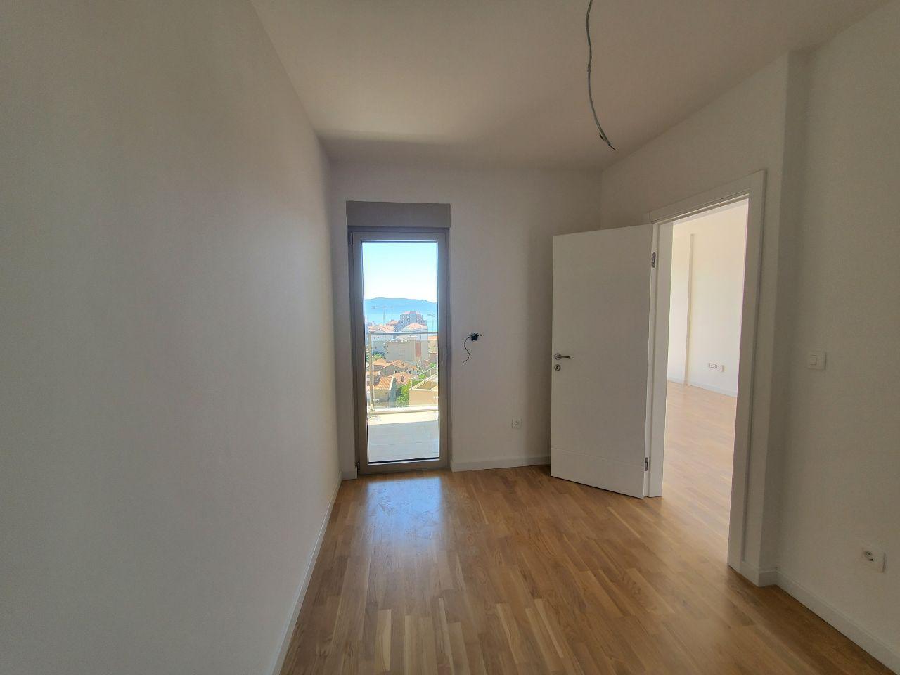 Bright bedroom with parquet flooring and access to a balcony in a residential building in Bečići, Montenegro, with sea and mountain views.
