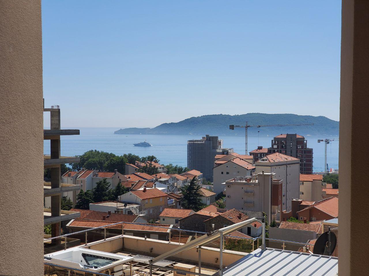 View from the balcony of the sea and the town of Bečići, Montenegro: a panorama of the coastline, red rooftops, and a yacht in the distance.