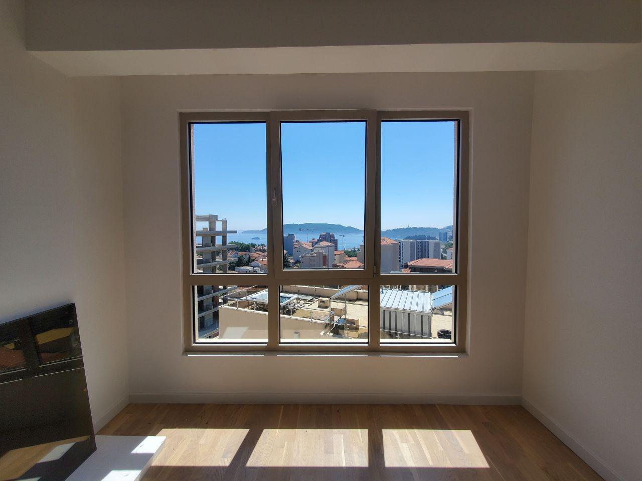 View from the living room window of the sea and the town of Bečići, Montenegro: a bright room with parquet flooring and panoramic glazing.