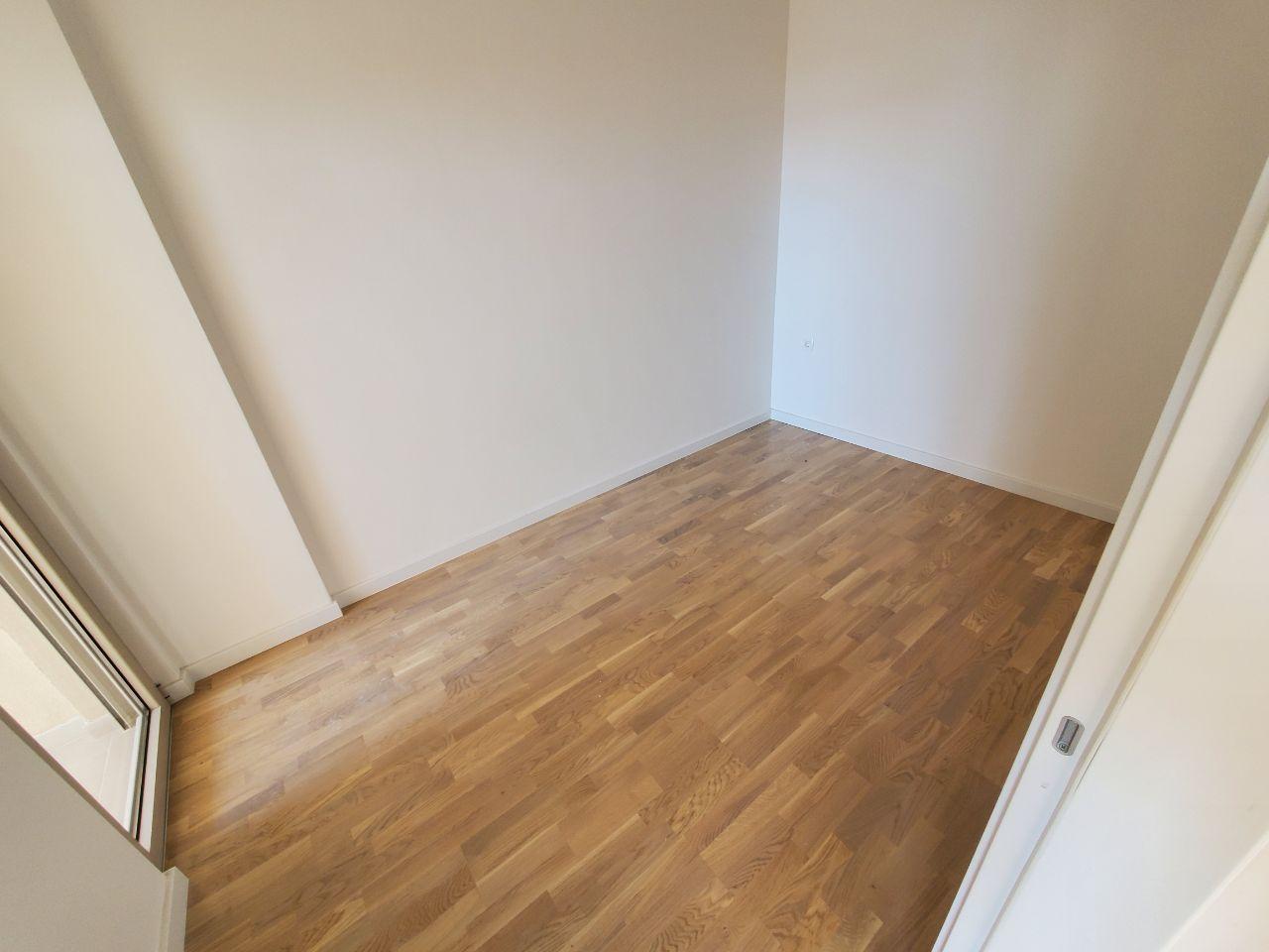 Bright empty bedroom with parquet flooring in a residential building in Bečići, Montenegro. View of the room entrance with a balcony.