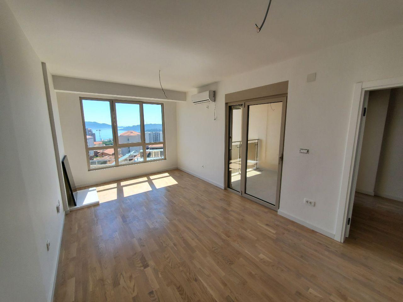 Bright living room with parquet flooring and panoramic sea views in a new residential building in Bečići, Montenegro.
