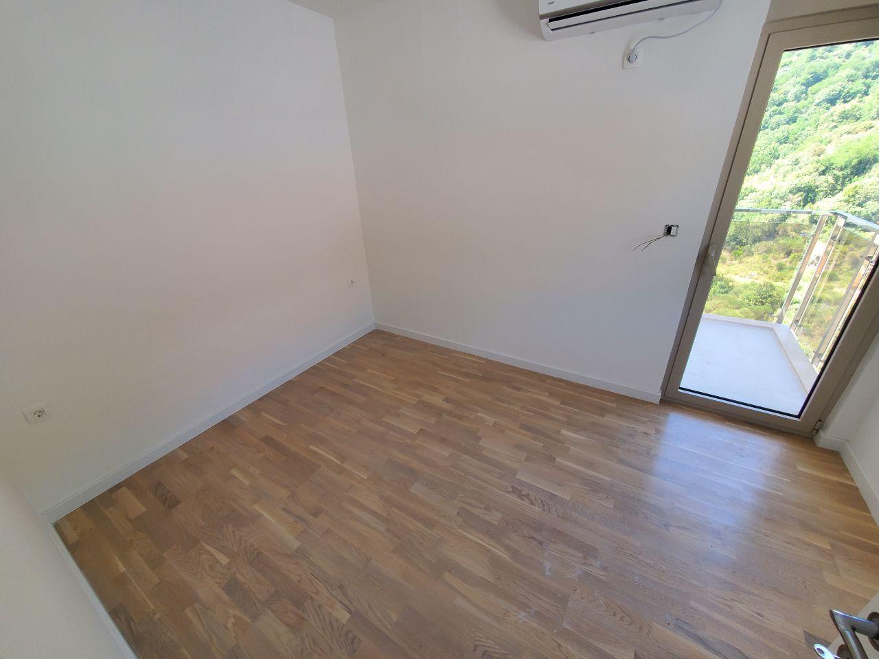 Bright bedroom with parquet flooring and access to a balcony in a residential building, Becici, Montenegro. View of green mountains from the window.