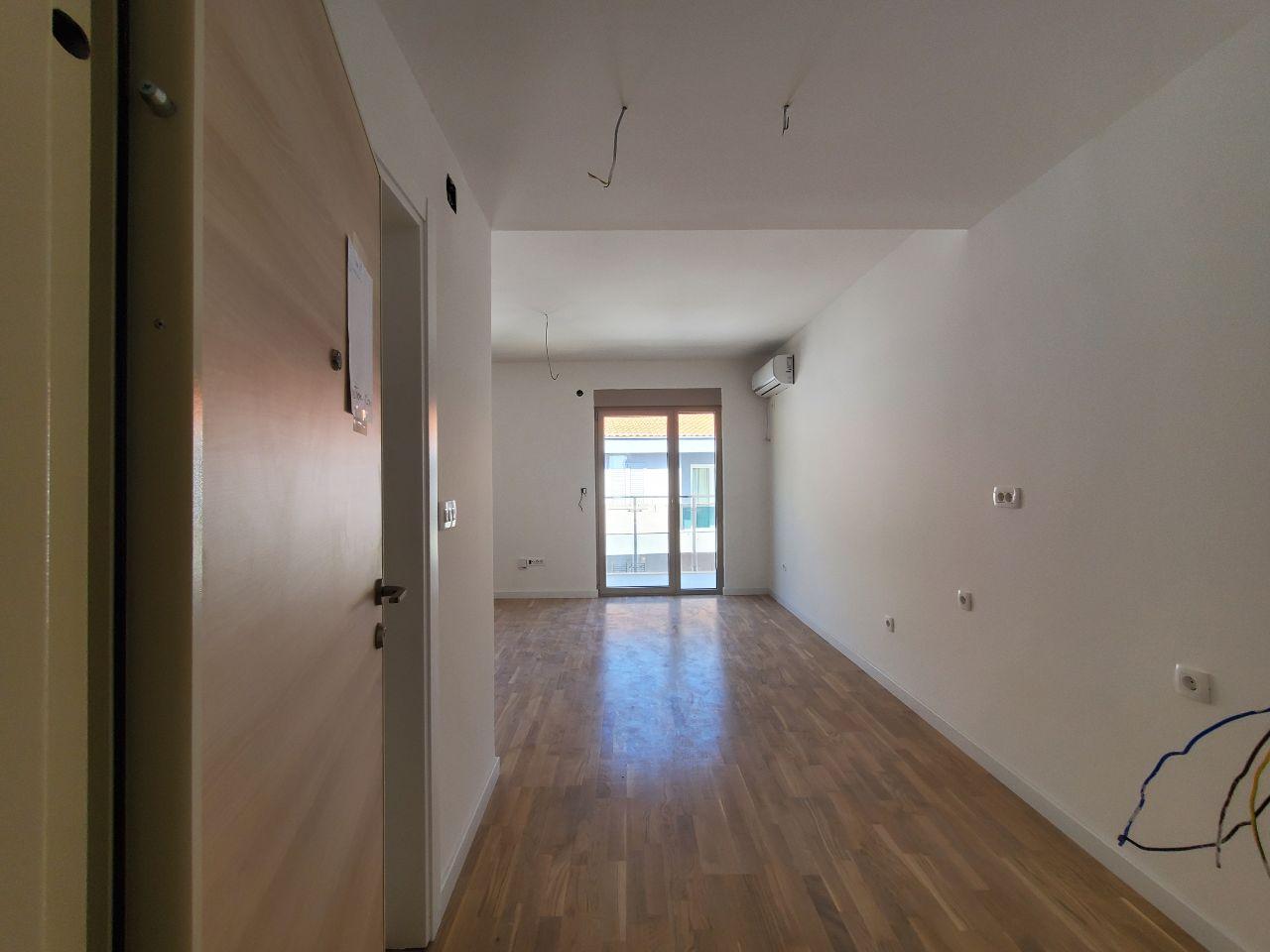 Bright living room in a new development in Bečići, Montenegro: parquet flooring, white walls, air conditioning, and access to the balcony.