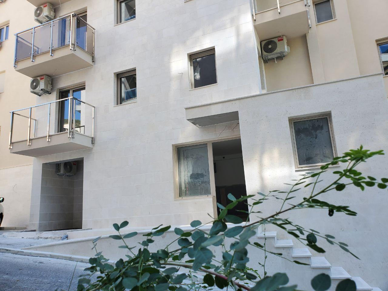 Facade of a modern residential building in Bečići, Montenegro: light stone cladding, glass balconies, and air conditioners.