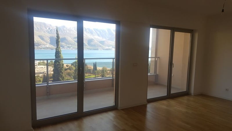 Living room with panoramic windows and a view of the sea and mountains in an apartment, Bečići, Montenegro. Parquet floor, access to the balcony.