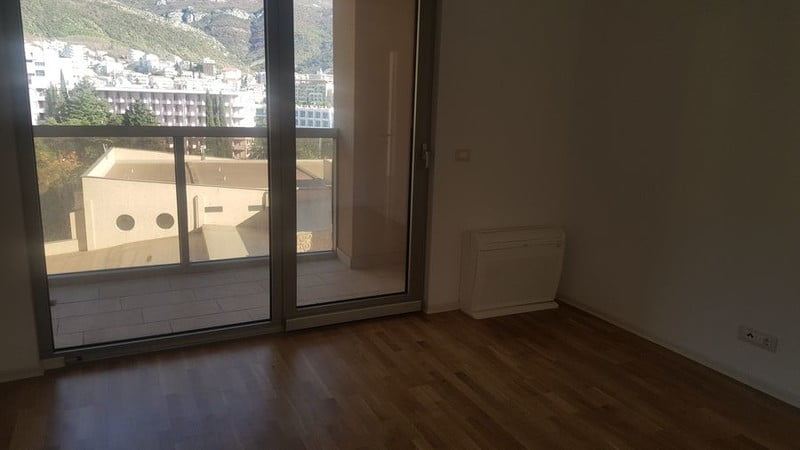 Bright living room with parquet flooring, a panoramic window, and access to the balcony in an apartment in Bečići, Montenegro.