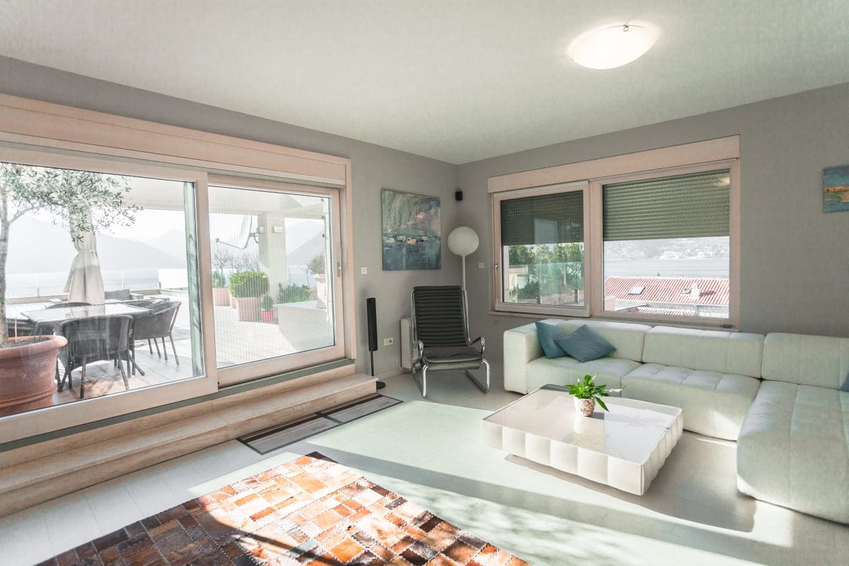 Bright living room in an apartment in Ljuta, Montenegro: white sofa, panoramic windows with sea view, and access to the terrace.