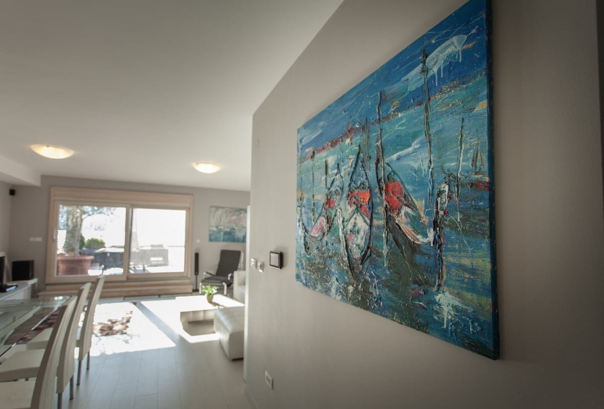 Modern living room with a painting in an apartment in Ljuta, Montenegro: bright interior, panoramic window, and dining area.