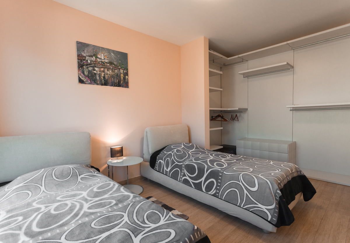 Bedroom with two beds and a built-in wardrobe in an apartment in Ljuta, Montenegro. Bright interior with a painting on the wall.