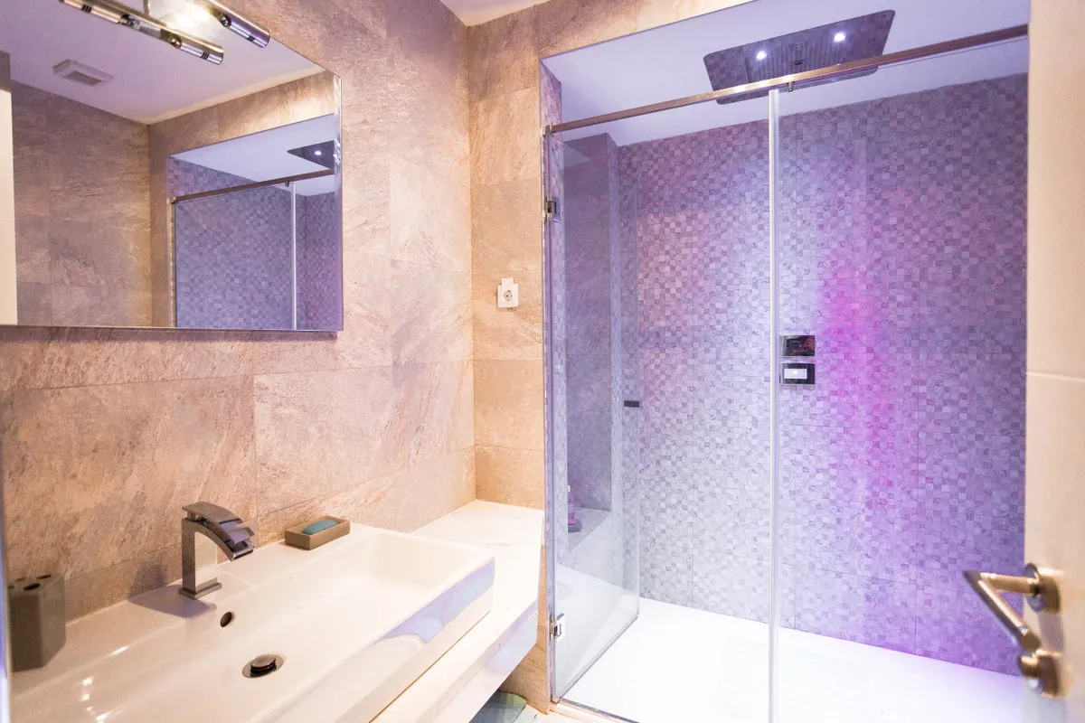 Modern bathroom featuring a white sink, large mirror, and glass shower enclosure with purple mosaic tiles.