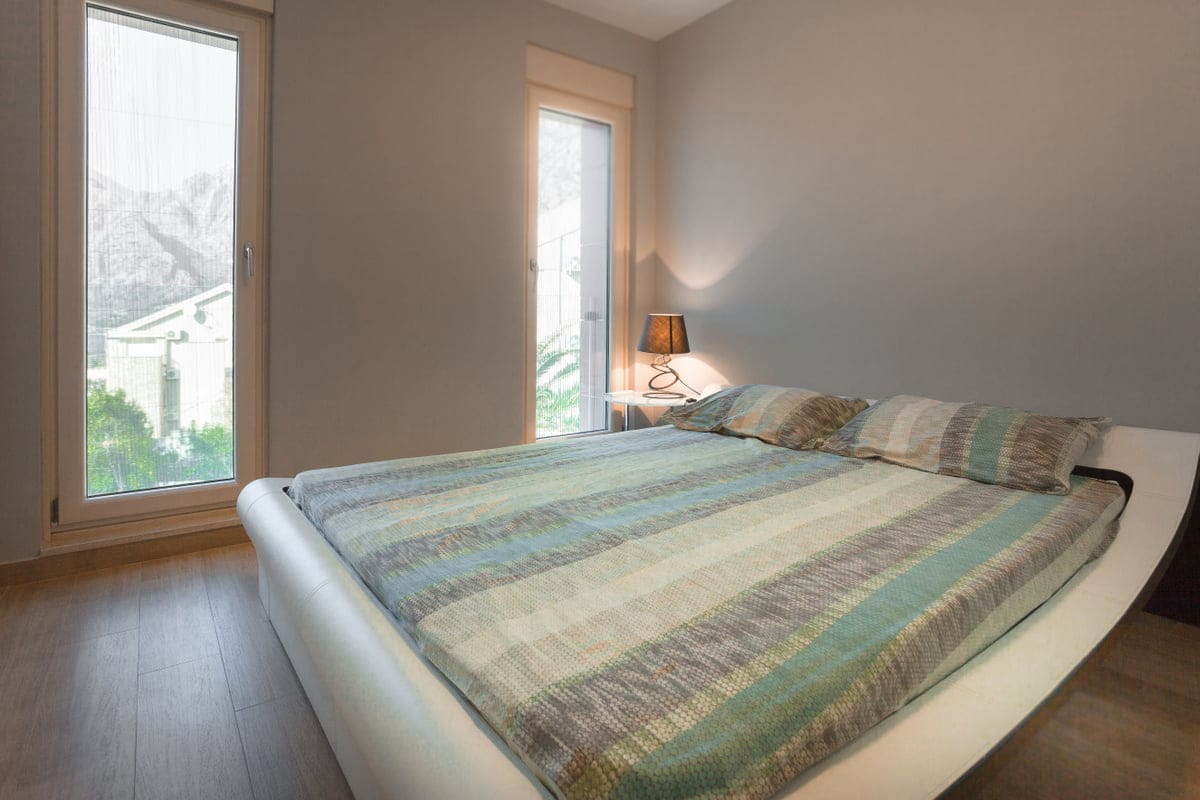 Modern bedroom with a double bed in an apartment in Ljuta, Montenegro, with panoramic windows and mountain views.