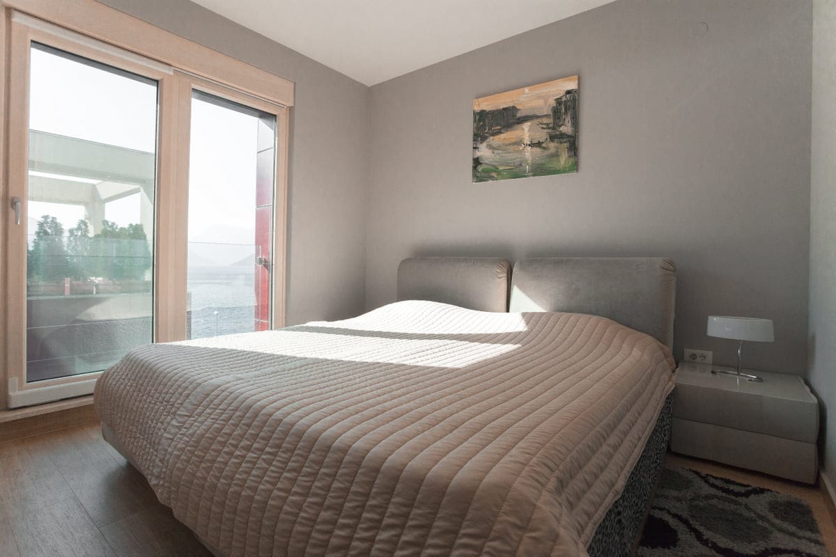 Bedroom in an apartment in Ljuta, Montenegro: a double bed, a panoramic window with a sea view, and a modern interior.