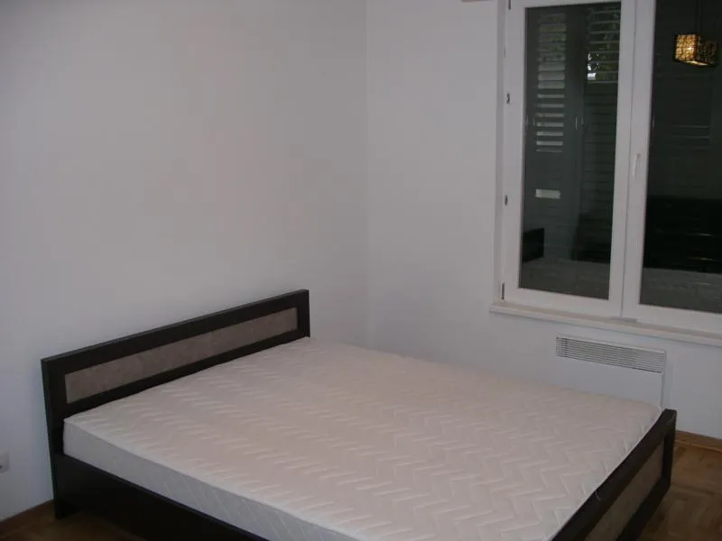 Bedroom with a dark wood bed frame and white mattress near a window with shutters.