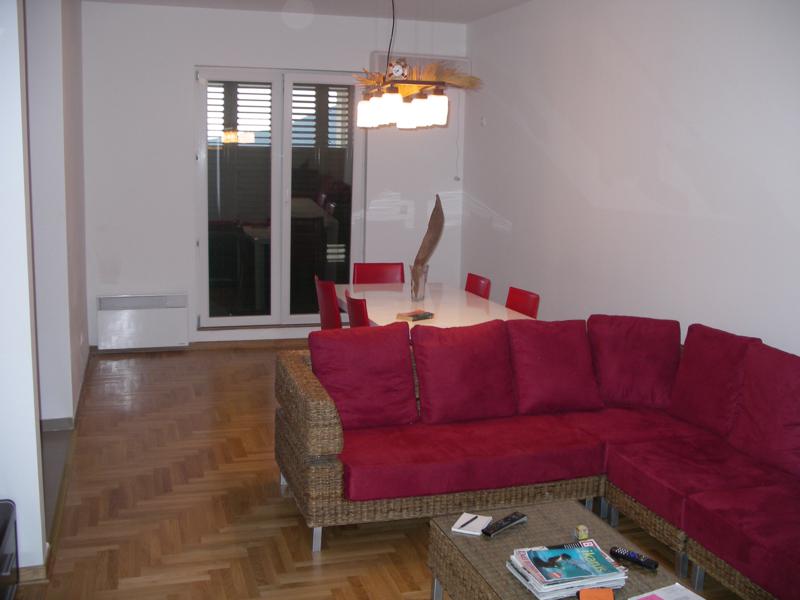 Living room with a wicker sofa and dining area in an apartment in Herceg Novi, Montenegro: parquet flooring, bright interior.