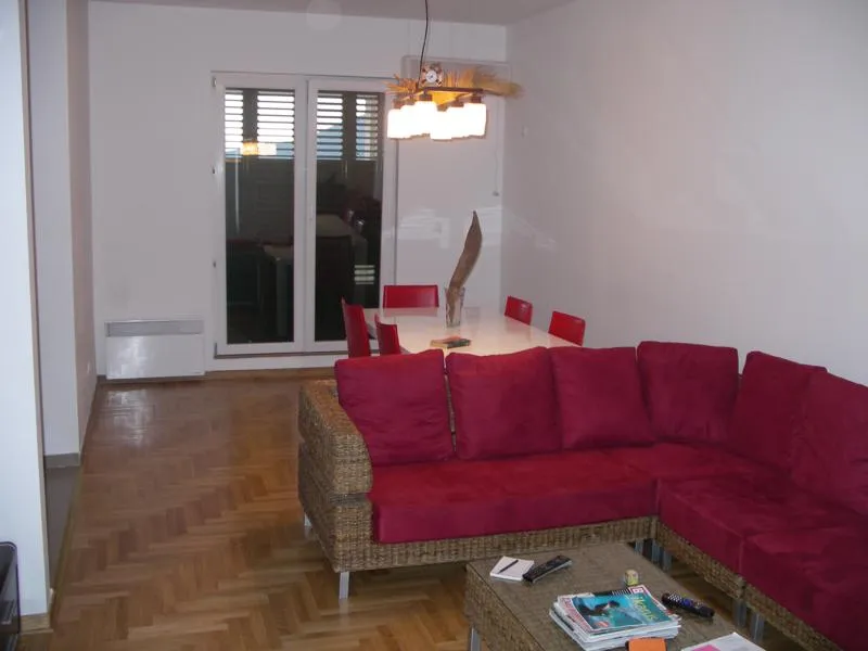 Living room featuring a red wicker sectional sofa, parquet flooring, and a dining area with red chairs in the background.