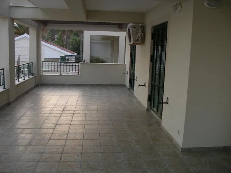 Covered balcony with tiled floor, metal railing, and louvered doors leading inside.
