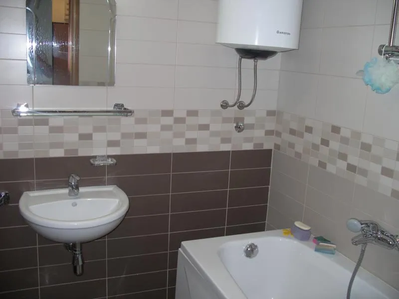 Bathroom featuring a sink, bathtub, wall-mounted water heater, mirror, and tiled walls.