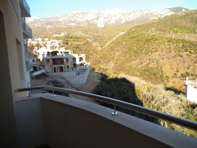 View from a balcony overlooking hills and unfinished construction. Metal railing visible.