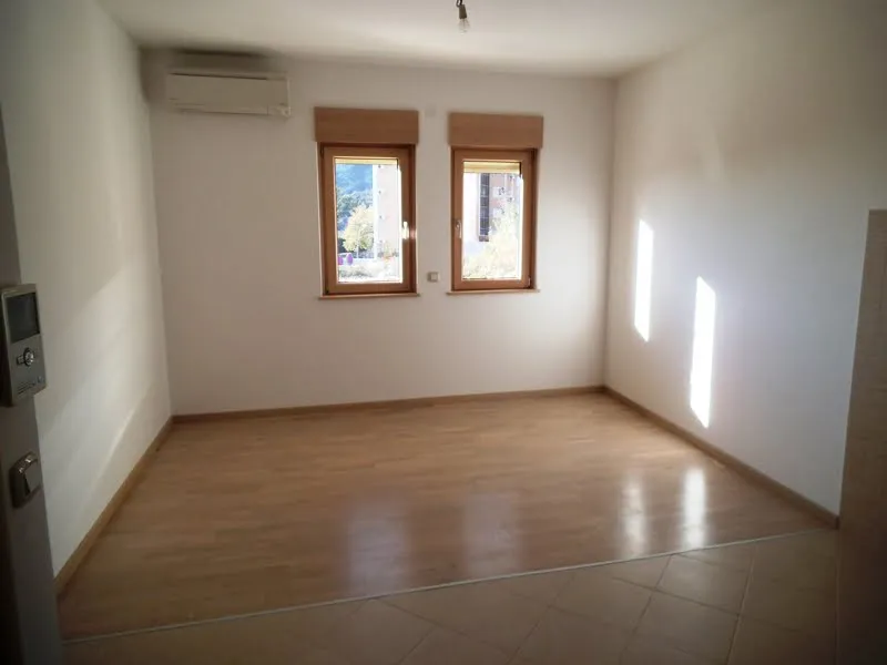 Empty room with laminate flooring, two windows, and a wall-mounted AC unit. Entry door with intercom visible.