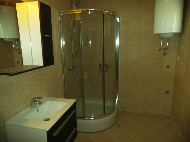 Bathroom in an apartment in Bečići, Montenegro: shower cabin, vanity with sink and boiler, finished with beige tiles.